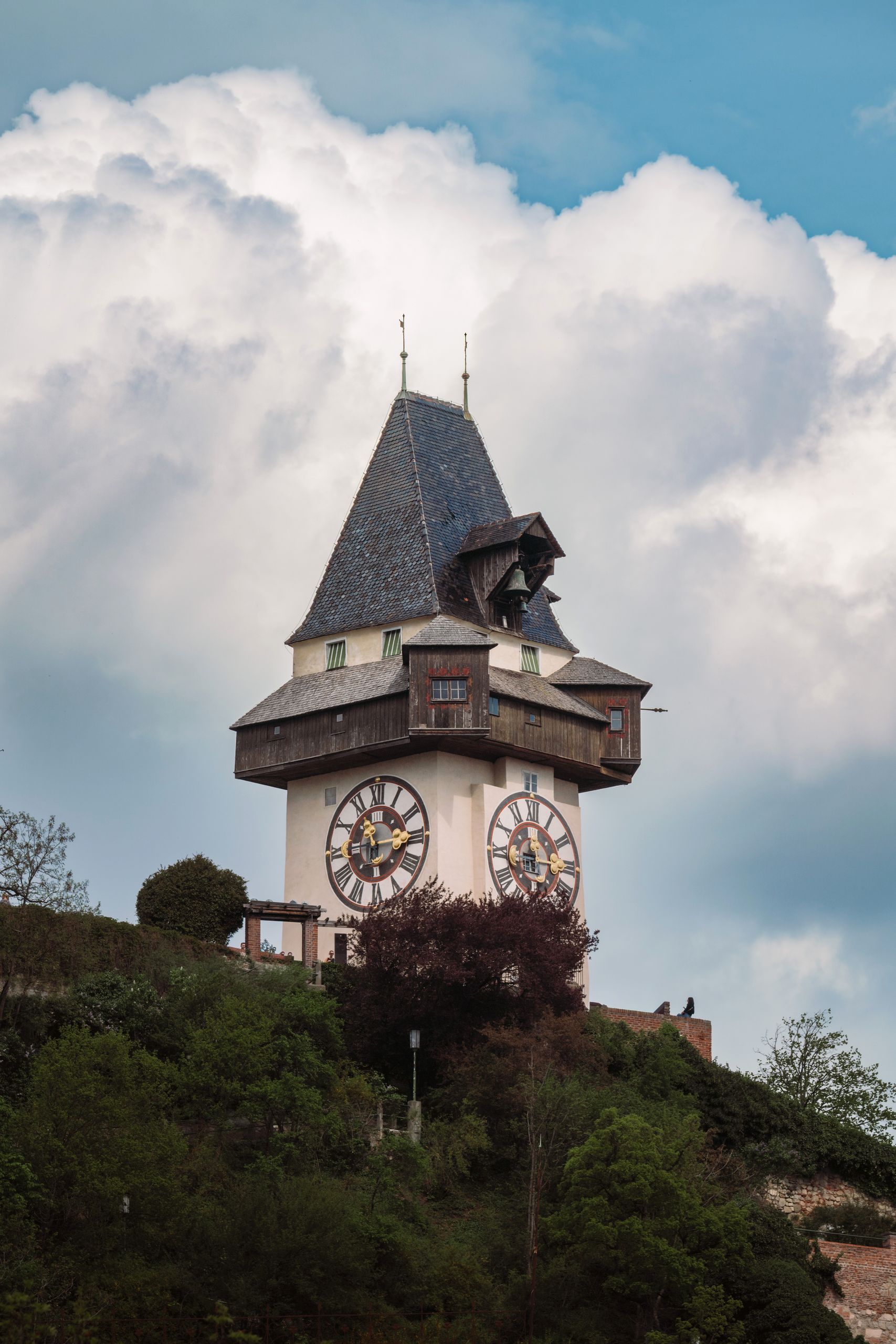 Up-close view of Graz's historic clock tower with a dramatic cloudy backdrop, showcasing Austrian heritage.